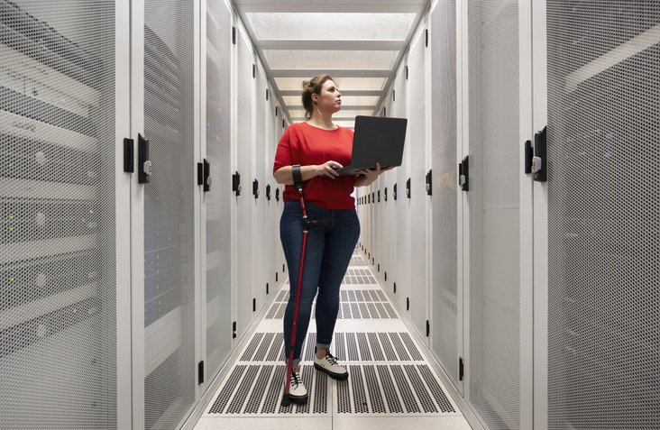 Engineer with physical disability holding laptop and working in server room at data center.