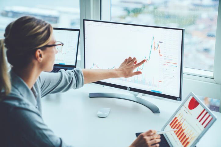 Female economist analyzing statistics graphs pointing on screen of computer at desktop.