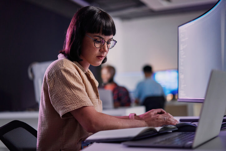 Female cybersecurity engineer typing on a digital tablet in an office server room.