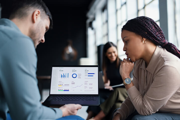 Two data scientists sitting in a modern office. They are collaborating on financial data analysis, discussing strategies and insights for their business goals and corporate objectives.