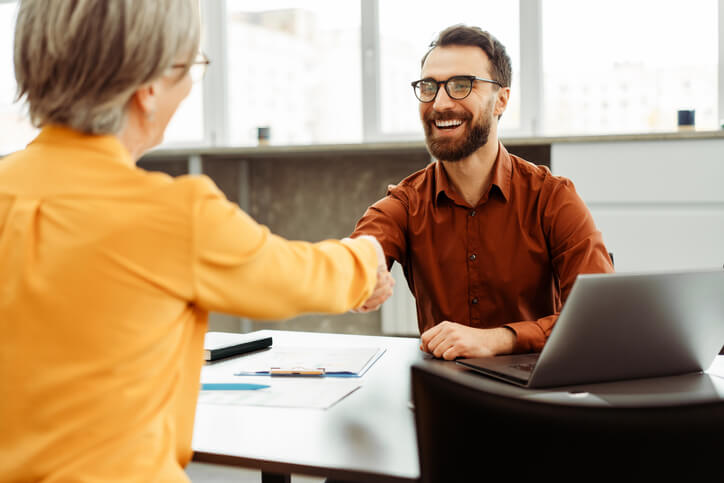 A male candidate smiles while greeting a female human resources manager during a job interview.