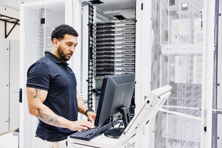 Male IT professional at a computer while configuring a server in an office data center.