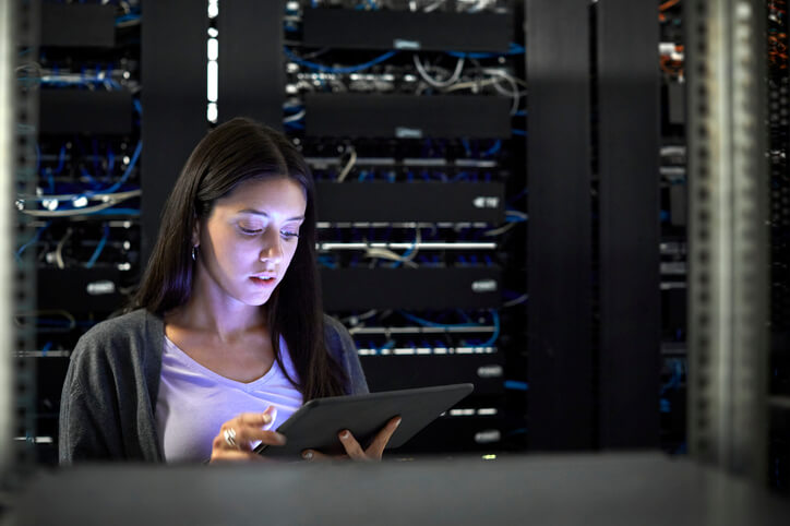 Female cybersecurity engineer typing on a digital tablet in an office server room.