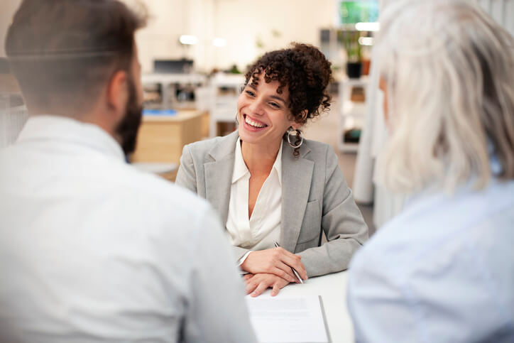 Cheerful female accountant having a meeting with two older clients at her desk in a banking office.