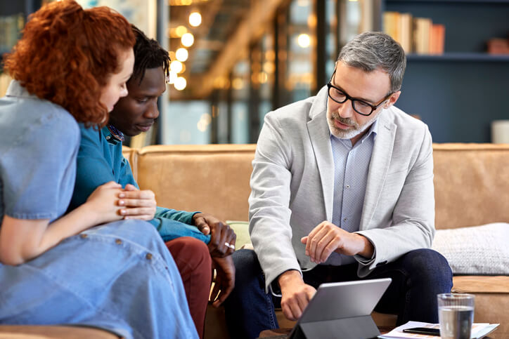 Senior male accountant talking personal finances with a young multi-ethnic couple at his office.
