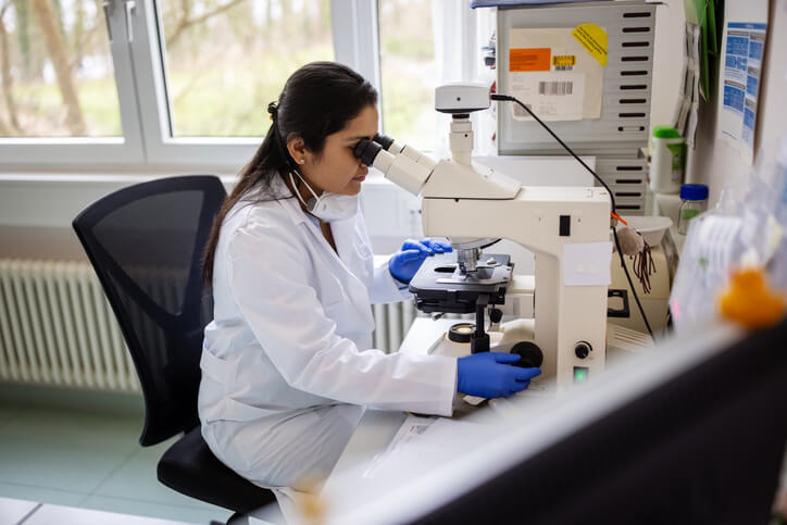 Woman wearing lab coat and protective face mask while working on research in the laboratory.
