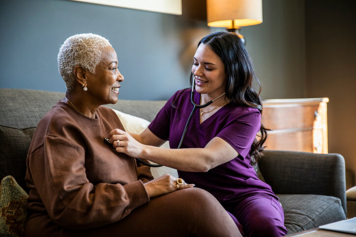 A female nurse checking a senior woman's vital signs in her home.