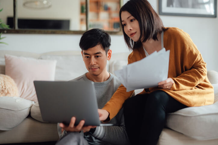 Young couple discussing over financial bills while using laptop on sofa.