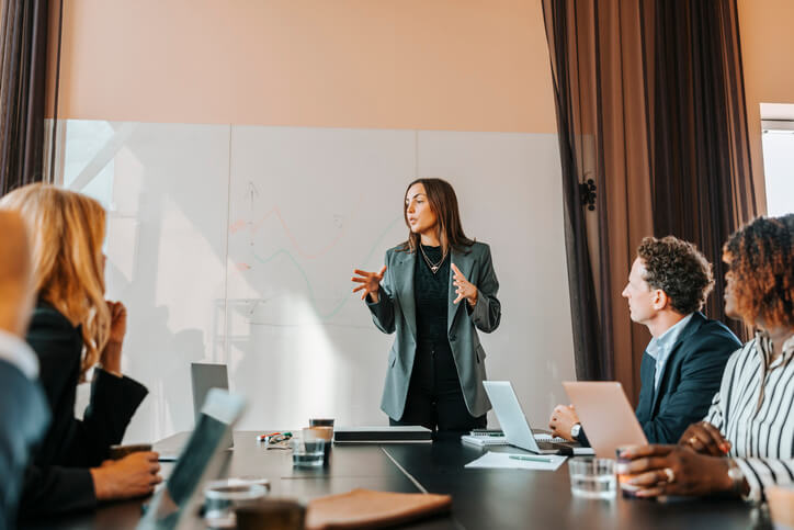 Female financial analyst explaining strategies to colleagues in a board room at the office.