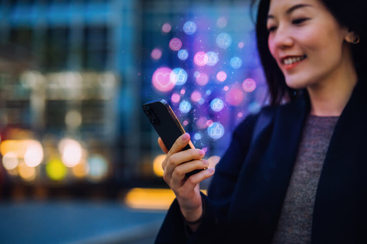 Asian woman using a social media app on her smartphone to give likes to friends' comments.