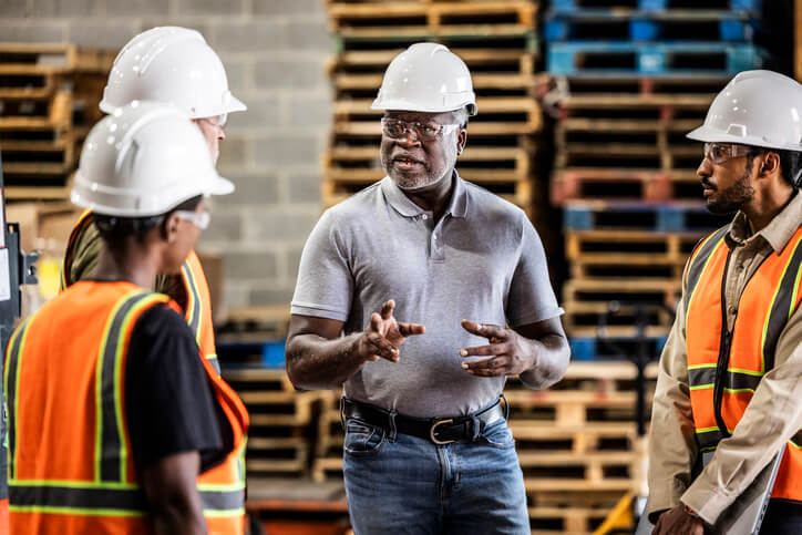 Supply chain supervisor speaking with a group of shipping warehouse employees.