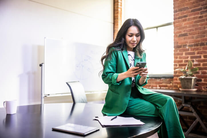 Asian American female marketer using a smartphone in a modern office conference room.