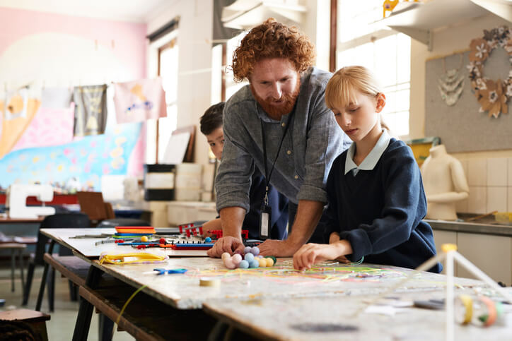 Male teacher helping a student using threads to make a project in art class at an elementary school.