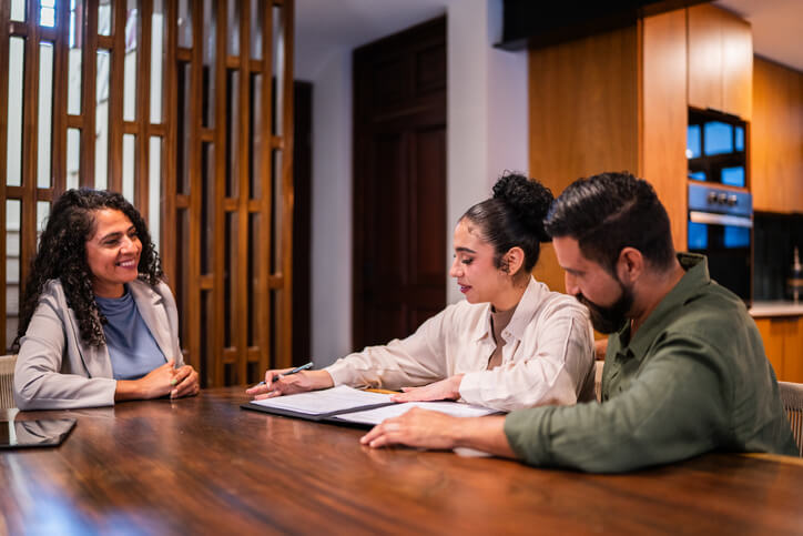 Spanish legal translator helping a couple interpret and sign documents at their home dining room table.