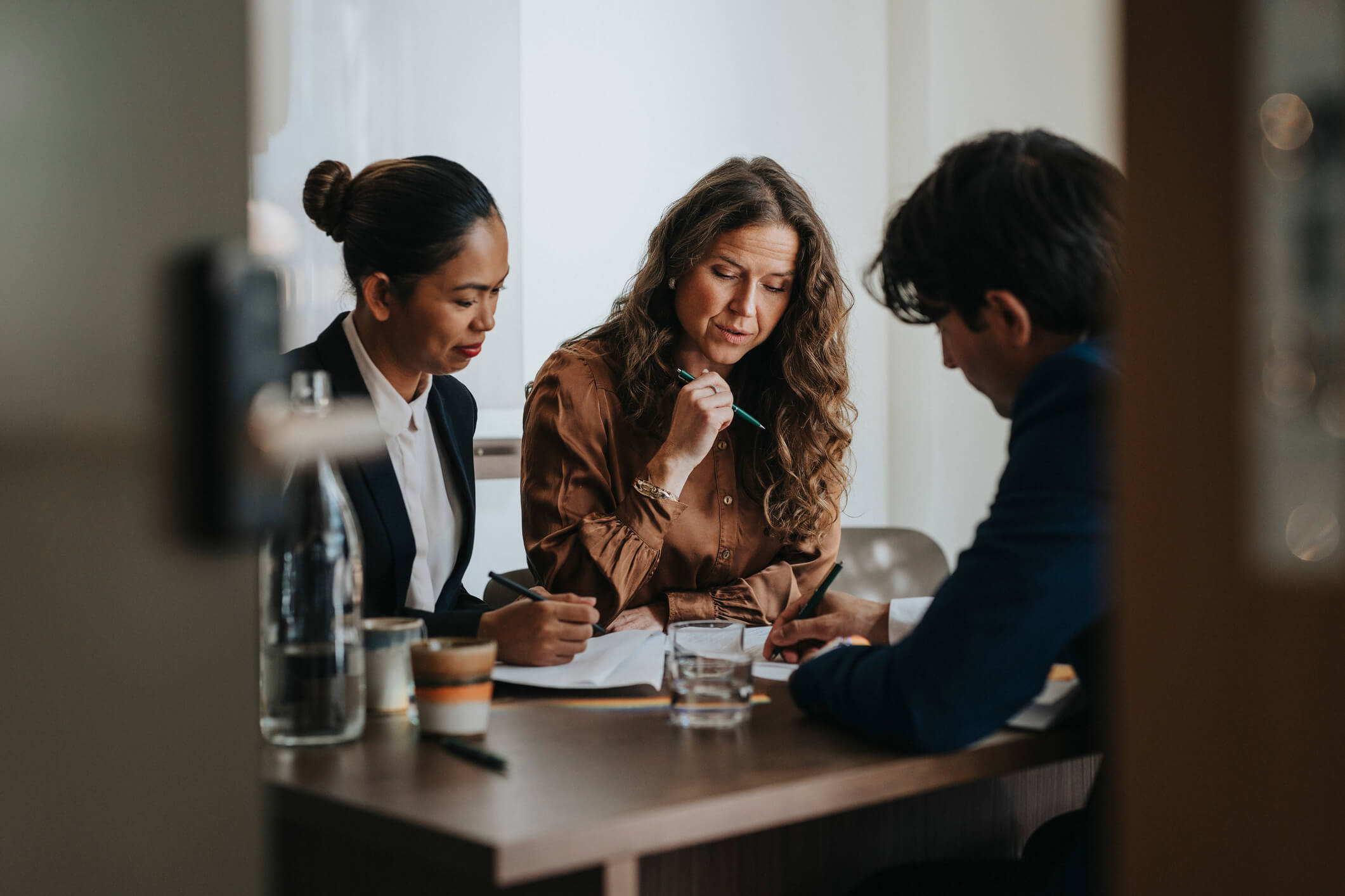 Young businessman writing while discussing strategy with female colleagues sitting at desk in office.