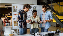Three-person team of computer programmers and video game designers having a meeting in the office, using a white board for brainstorming and ideas.